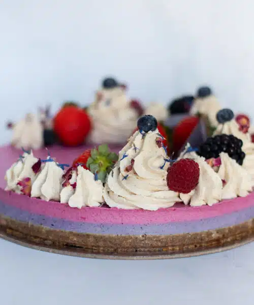 Raw Passion Berrylicious Cake surrounded by fresh strawberries, blueberries & blackberries in a bright, summery setting