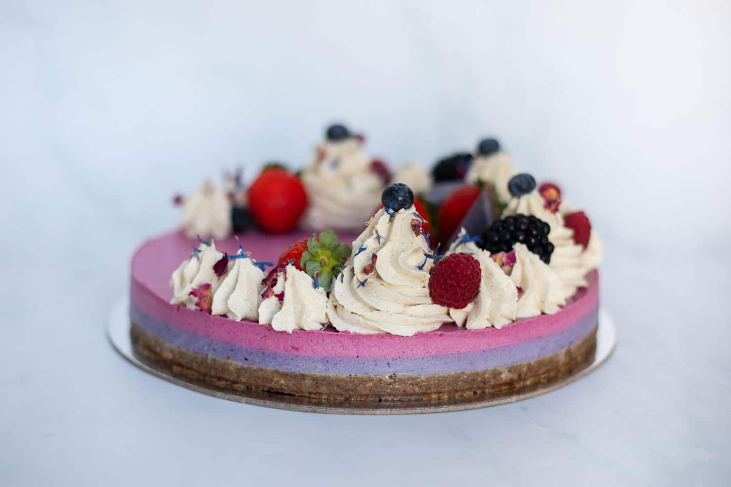 Raw Passion Berrylicious Cake surrounded by fresh strawberries, blueberries & blackberries in a bright, summery setting