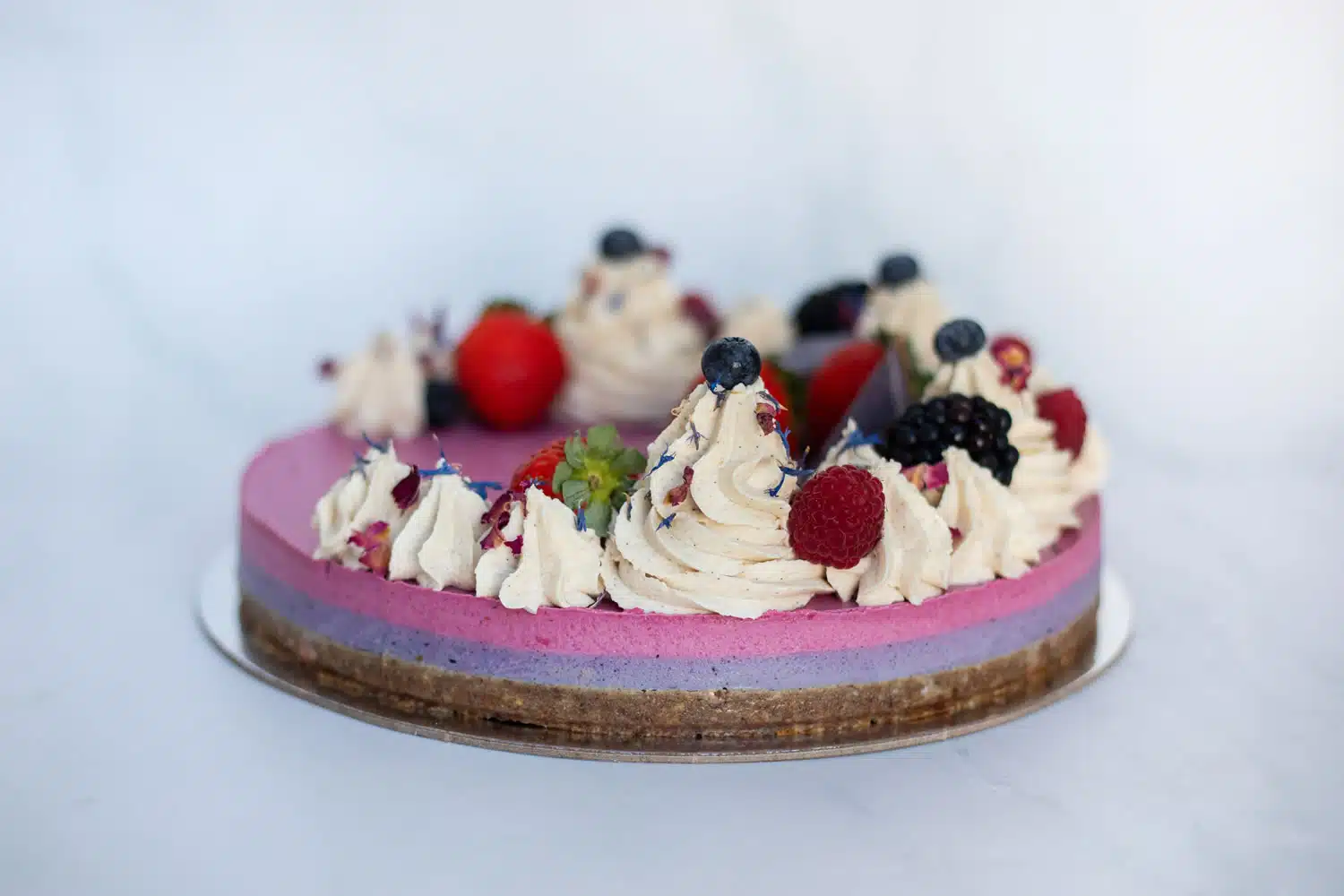 Raw Passion Berrylicious Cake surrounded by fresh strawberries, blueberries & blackberries in a bright, summery setting