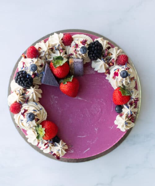 A slice of Berrylicious Cake on a plate showing colourful berry layers and smooth vanilla frosting
