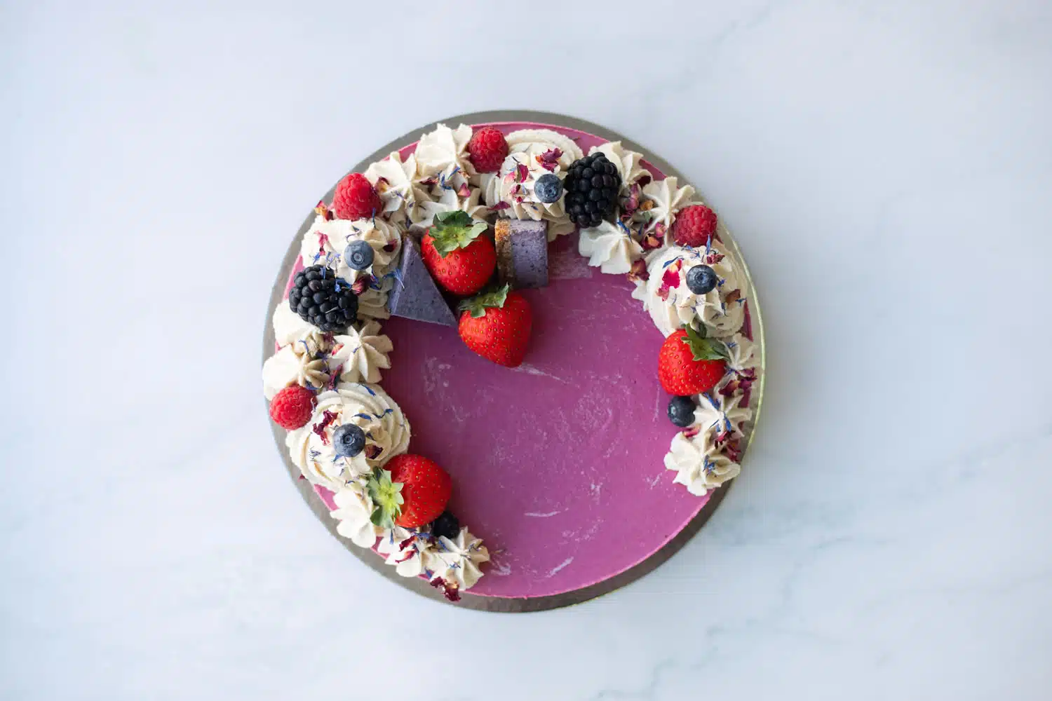 A slice of Berrylicious Cake on a plate showing colourful berry layers and smooth vanilla frosting